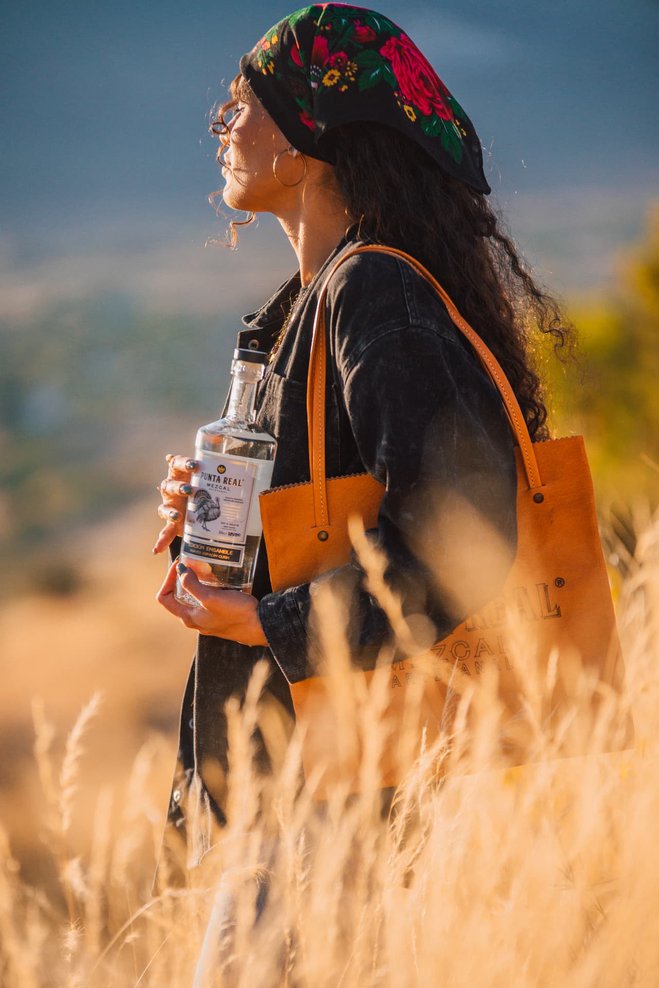 Mujer con botella de Punta Real en un campo de maguey al atardecer